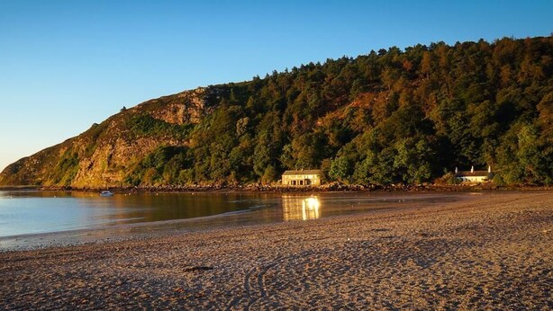 A beach with a building on a hill, calm water, and boats. - 4 Bed in Llanbedrog (oc-sunnyd) (Llanbedrog)