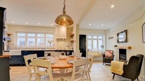Een ruime keuken met een centraal eiland, witte stoelen en een eettafel voor zes personen.