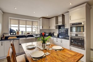 A modern kitchen with white cabinets, a wooden dining table set for two, and a built-in oven. - 3 Bed in Pantglas (oc-bow24) (Pant Glas)