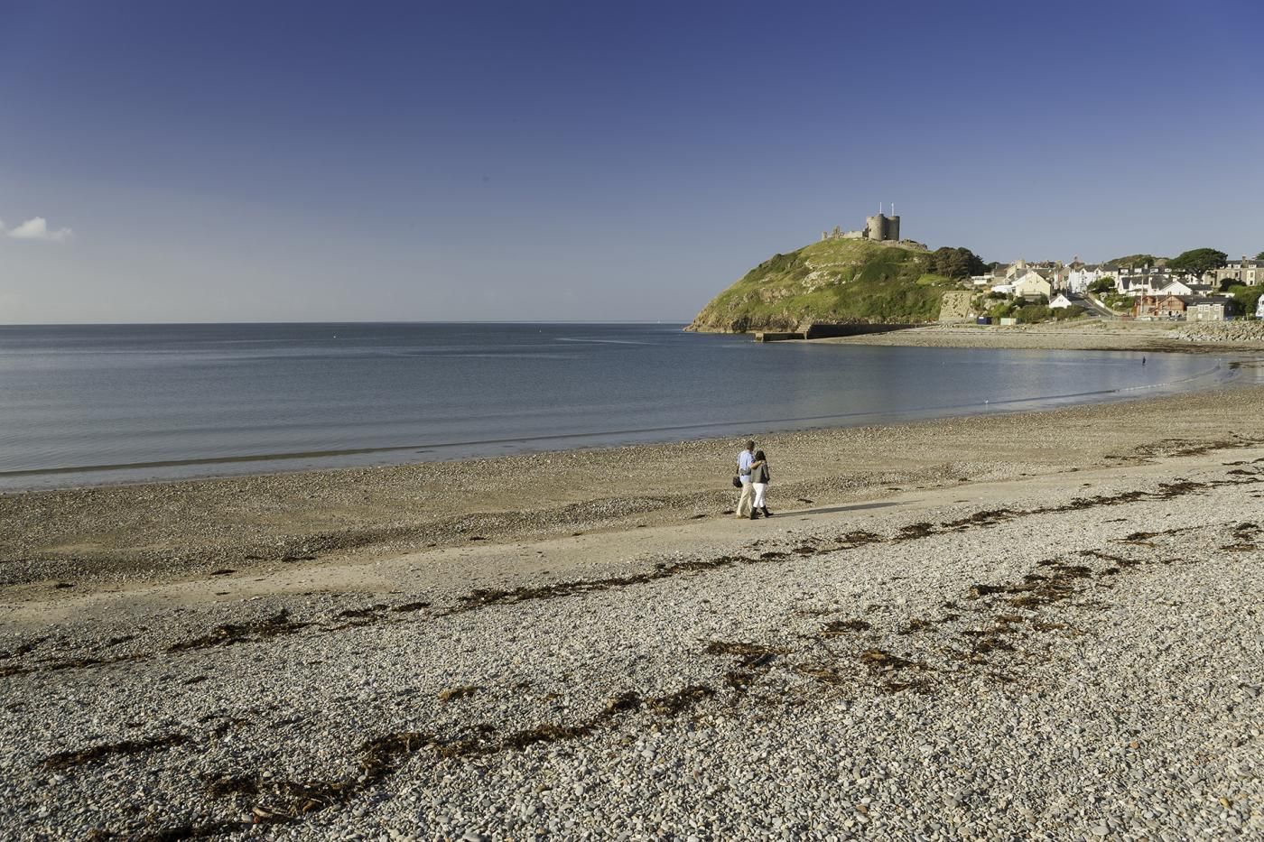 A pebbly beach with a castle on a hill in the background.