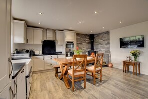 A modern kitchen with white cabinets, a black countertop, and a wooden dining table with chairs. - 3 Bed in Pantglas (oc-bow24) (Pant Glas)