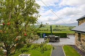 A stone building with a patio area, a table with chairs, and a view of rolling hills. - 3 Bed in Pantglas (oc-bow24) (Pant Glas)