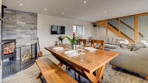 Ein moderner Essbereich mit einem Holztisch, gedeckt für vier Personen, einem Kamin und einer Treppe zu einer oberen Ebene.