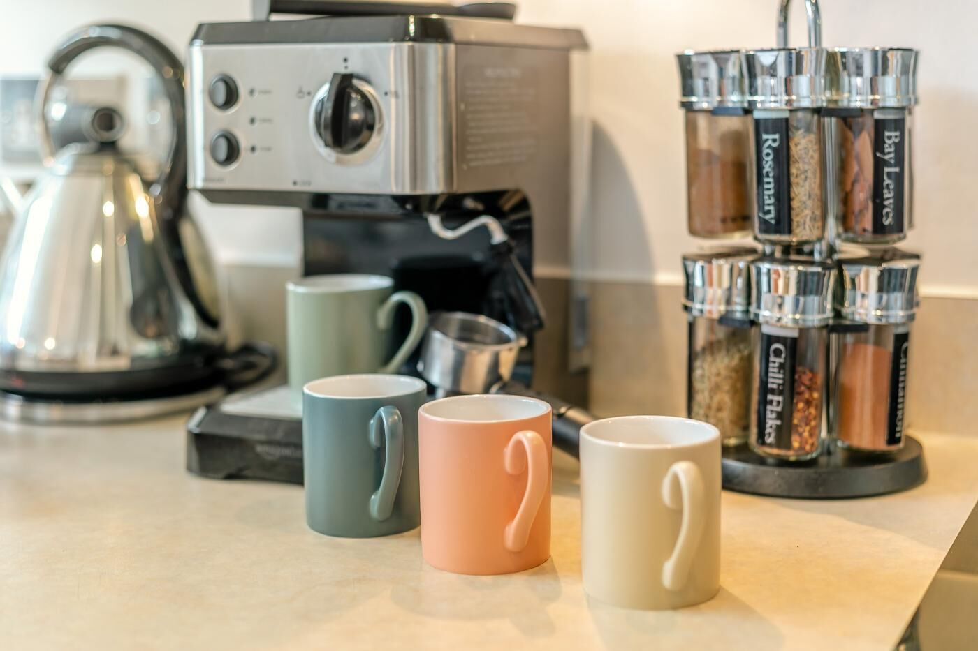 En køkkenbordplade med kaffemaskine, elkedel og en stabel krydderiglas.