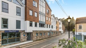 Un immeuble à plusieurs étages, avec un café au rez-de-chaussée, une façade en pierre et un mélange de panneaux extérieurs en bois et blancs.