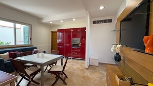 Una cocina moderna con armarios rojos, un comedor con mesa y sillas, y un televisor montado en la pared.
