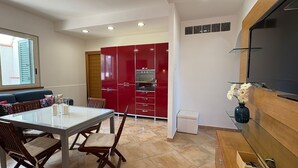 Una cocina moderna con armarios rojos, horno empotrado y comedor con mesa de vidrio y sillas de madera.