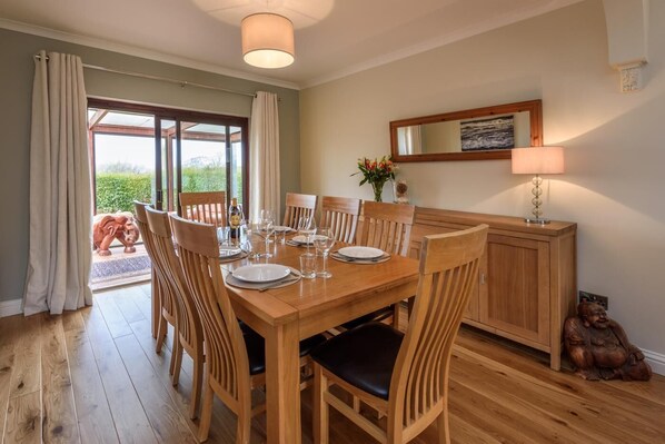 A dining room with a wooden table set for six, surrounded by wooden chairs. - 3 Bed in Tudweiliog (oc-1brodw) (Tudweiliog)