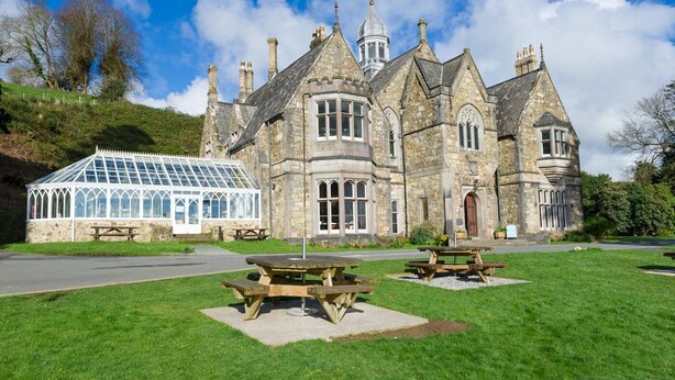 A historic stone building with a conservatory and picnic tables in a grassy area. - 3 Bed in Llanbedrog (oc-thehol) (Llanbedrog)