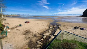 A beach with a rocky shoreline, a clear sky, and distant mountains. - 3 Bed in Llanbedrog (oc-thehol) (Llanbedrog)