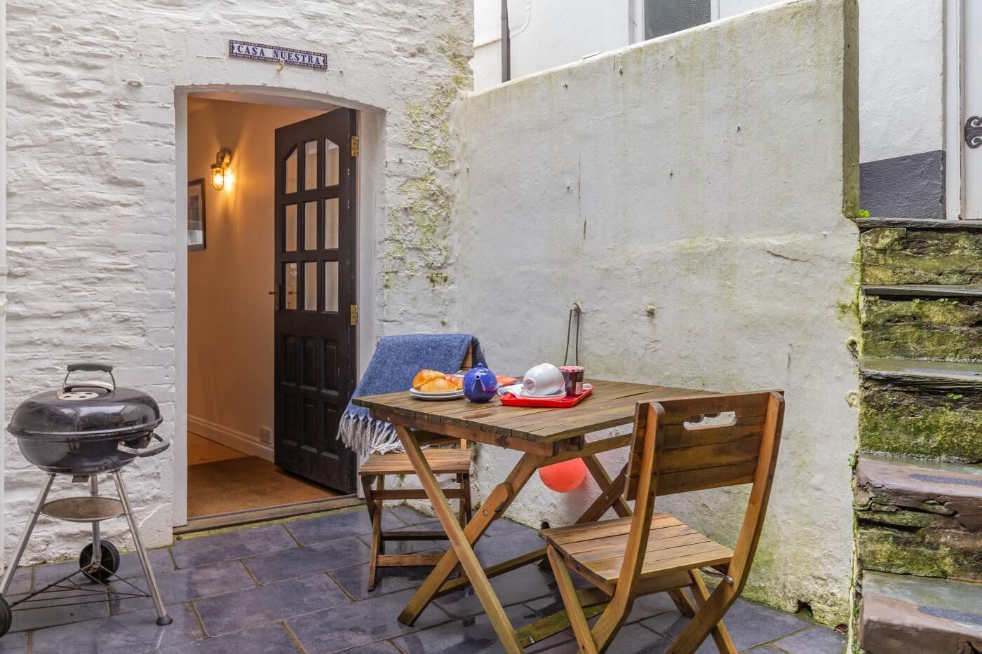 Zona d'estar a l'aire lliure amb estil rústic, que inclou taula i cadires de fusta, una barbacoa i un cartell que diu "CASA NUESTRA".