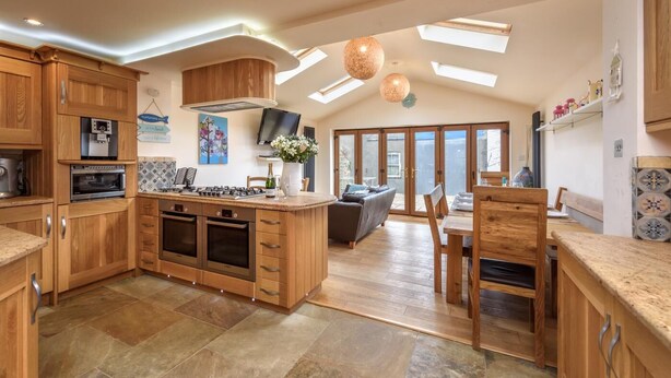 A spacious kitchen with wooden cabinets, a central island, and a dining area with a table and chairs. - 4 Bed in Mynytho (oc-angmyn) (Mynytho)