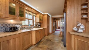 A kitchen with wooden cabinets, a stone floor, and a coffee machine. - 4 Bed in Mynytho (oc-angmyn) (Mynytho)