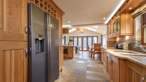 A modern kitchen with wooden cabinets, a stainless steel refrigerator, and a stone tile floor. - 4 Bed in Mynytho (oc-angmyn) (Mynytho)