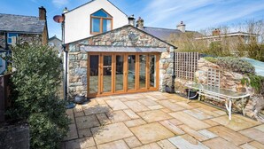 A stone conservatory with glass doors, a stone exterior, and a patio area with stone tiles. - 4 Bed in Mynytho (oc-angmyn) (Mynytho)
