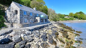 A stone house with a sloped roof, located on a rocky shoreline with a view of the sea. - 2 Bed in Llanbedrog (oc-2thebo) (Llanbedrog)
