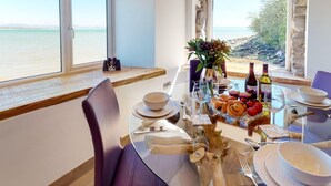 A dining table set for two with a view of the sea, a vase with flowers, and a bottle of wine. - 2 Bed in Llanbedrog (oc-2thebo) (Llanbedrog)