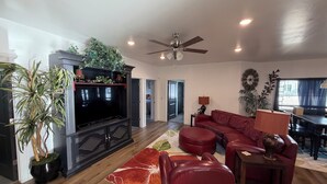 A living room with a flat-screen TV, red leather sofa, and a ceiling fan. - Cozy & Comfy Mountain-View Home Airport 15 min (West Valley City)