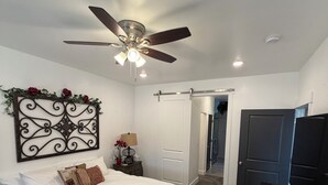 A bedroom with a bed, a ceiling fan, a decorative wall piece, a nightstand with a lamp, and a dresser with a TV. - Cozy & Comfy Mountain-View Home Airport 15 min (West Valley City)