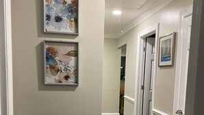 A hallway with two framed floral artworks on the wall, a wooden floor, and white doors. - Peaceful 3BR NW Raleigh Ranch Home. Pet friendly, RDU, UNC/Rex, Crabtree Mall (Raleigh)