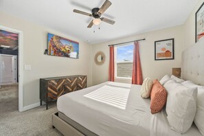 A bedroom with a bed, a ceiling fan, a herringbone-patterned cabinet, and a window with curtains. - *Arcade Games*Theme Rooms*Pvt Pool*Cinema Seats* (Kissimmee)