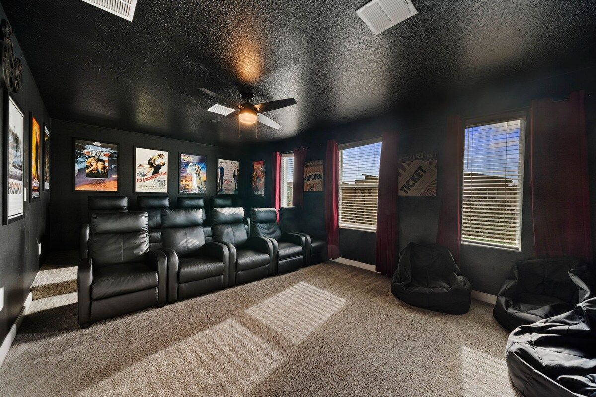 A home theater room with a ceiling fan, black leather recliners, a bean bag, and movie posters on the wall.
