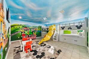A children's playroom with a slide, Mickey Mouse-themed wall art, and a seating area with a view of the outdoors. - *Arcade Games*Theme Rooms*Pvt Pool*Cinema Seats* (Kissimmee)