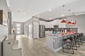 A modern kitchen with a central island, bar stools, stainless steel appliances, and pendant lighting. - *Arcade Games*Theme Rooms*Pvt Pool*Cinema Seats* (Kissimmee)