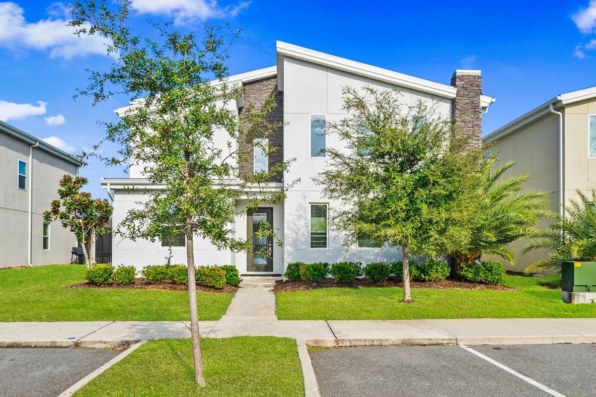 A modern two-story residential building with a central entrance, surrounded by well-maintained lawns and trees.