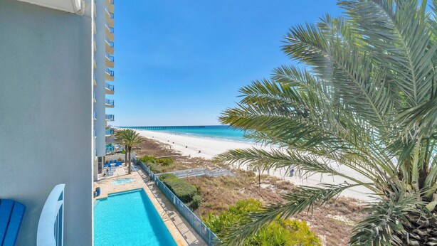 Un balcone con vista sulla spiaggia, una piscina e una palma.