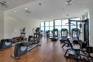 Ein großzügiger Fitnessraum mit verschiedenen Cardiogeräten, Kraftstationen und einem großen Fenster mit Blick ins Freie.