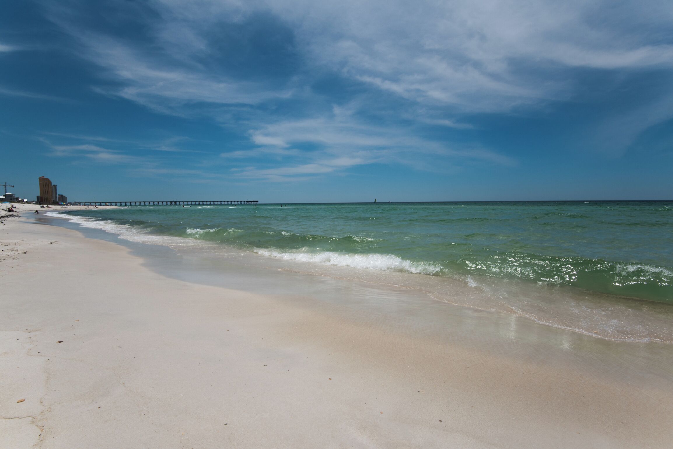 A beach with a pier extending into the ocean, sandy shore, and clear blue sky.