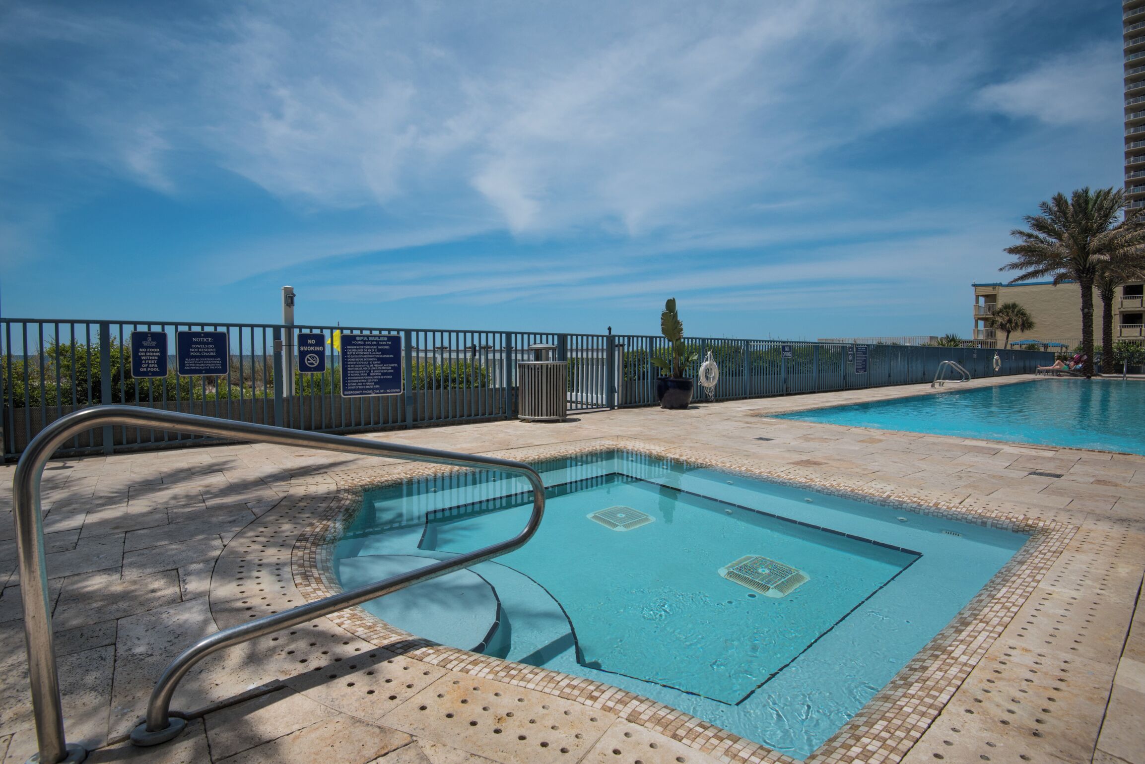 Piscina com guarda-corpo de metal, cercada por uma vedação com placas informativas.