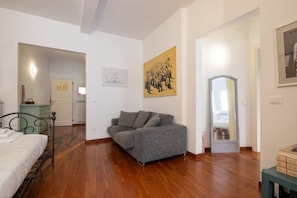 Une chambre à coucher avec un lit, un canapé gris, un plancher en bois, un miroir et un tableau accroché au mur.