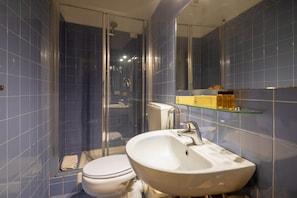 Une salle de bain avec une douche à parois de verre, des toilettes blanches et un lavabo blanc avec une étagère en verre au-dessus.
