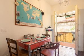 Un coin repas agrémenté d’une carte du monde au mur, d’une table dressée pour quatre personnes et d’une vue sur un balcon doté d’un toit en tuiles.