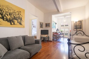Un salon avec un canapé gris, un cadre de lit en métal noir et une œuvre d’art jaune accrochée au mur.