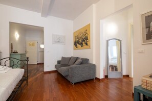 A bedroom with a bed, a grey sofa, a wooden floor, a mirror, and a painting on the wall. - San Niccolò Elegant Apartment (Florence)