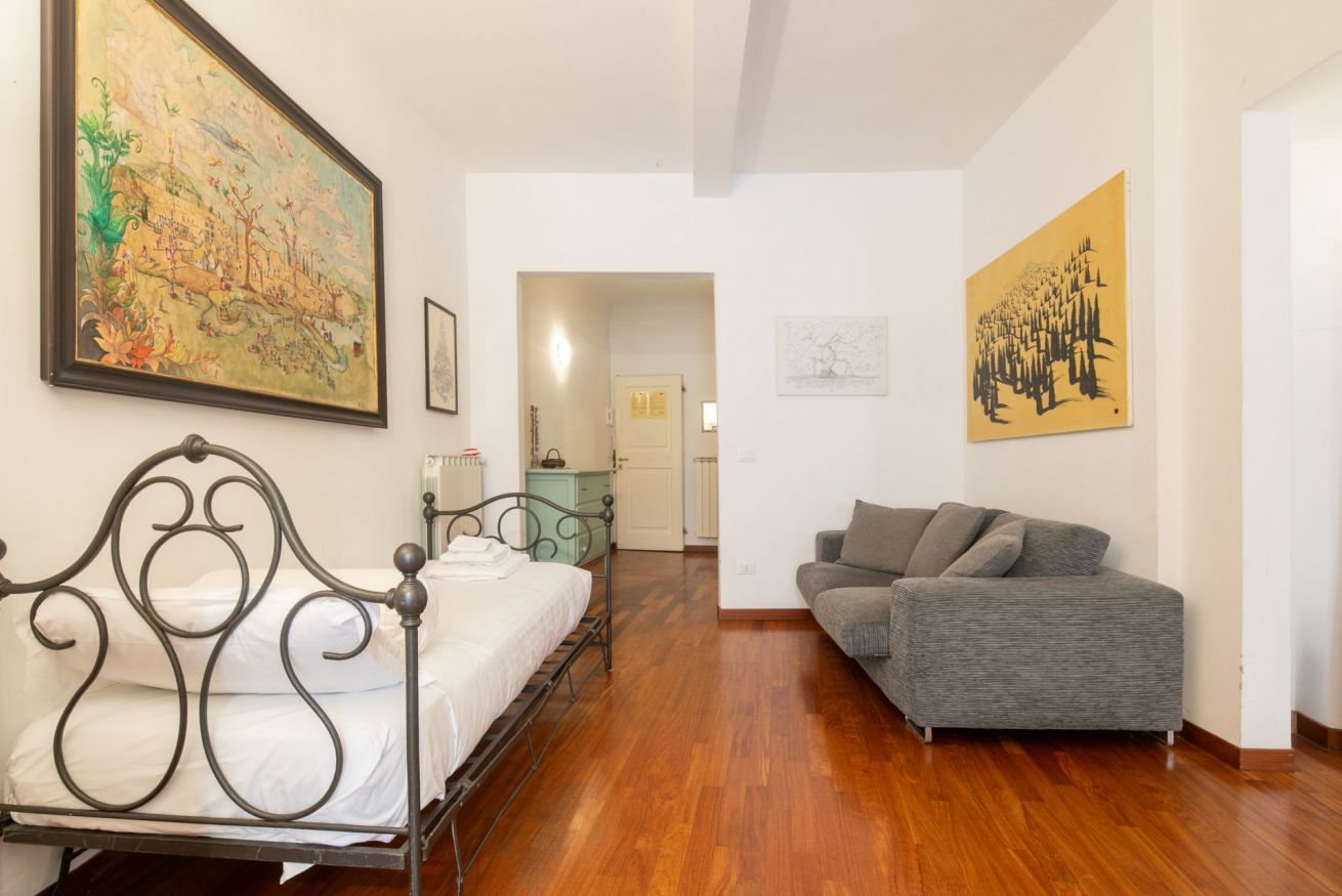 A bedroom with a metal bed frame, a gray sofa, and two paintings on the walls.