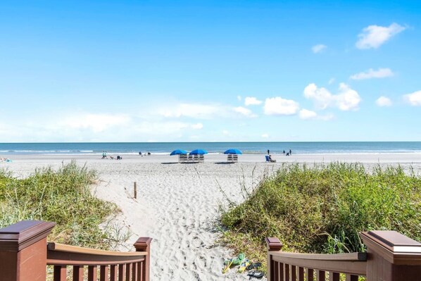 A beach with a wooden walkway leading to the water, a few umbrellas, and people in the distance. - 3 Bdrm North Shore Villa w/ Lazy River, Hot Tub (North Myrtle Beach)