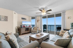 Ein geräumiges Wohnzimmer mit einer großen Couch, einem Couchtisch und einem Fernseher. Es gibt einen Balkon mit Meerblick.