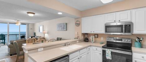 A modern kitchen with white cabinets, stainless steel appliances, and a view to the outside.