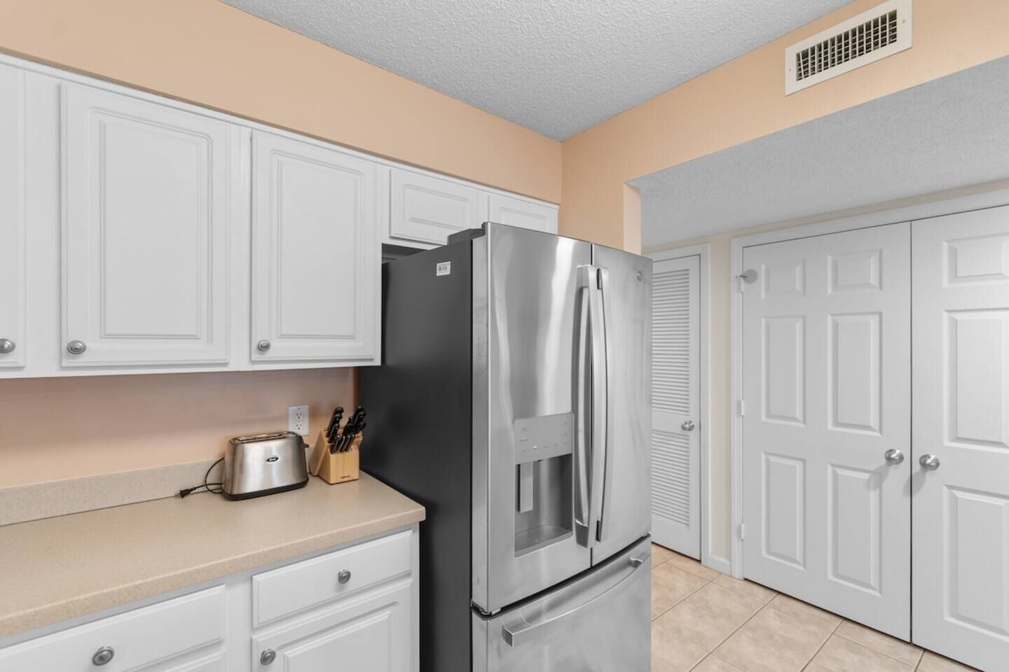 A kitchen with white cabinets, a stainless steel refrigerator, a toaster, and a knife block.