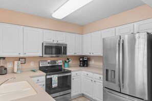 A modern kitchen with white cabinets, stainless steel appliances including a microwave, oven, and refrigerator, and a countertop with a coffee maker and other items. - 3 Bdrm North Shore Villa w/ Lazy River, Hot Tub (North Myrtle Beach)