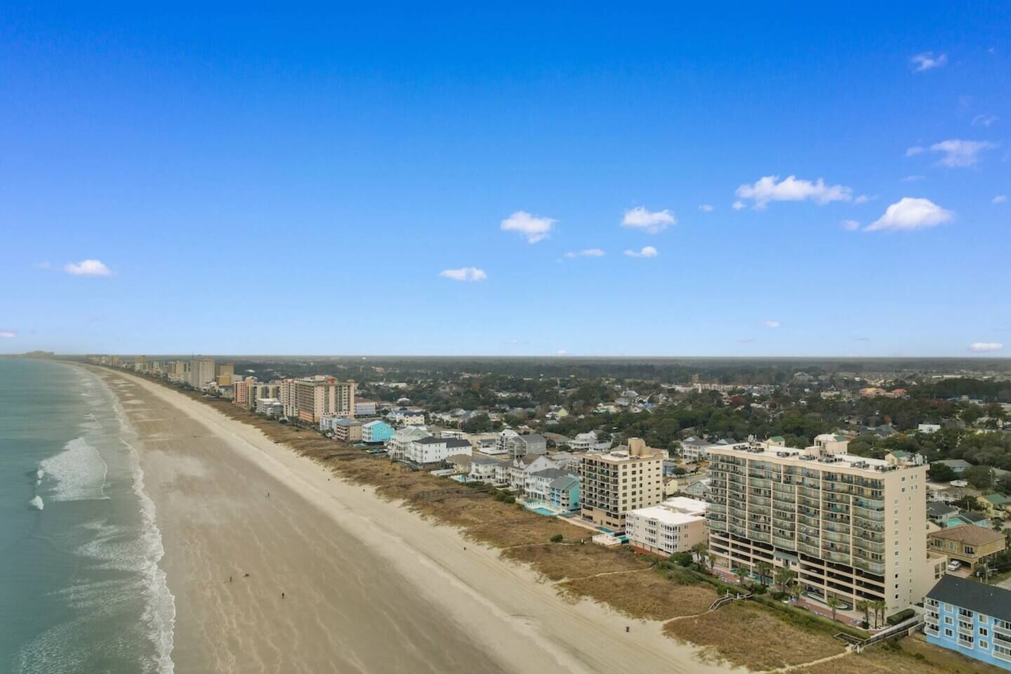 A coastal cityscape with a beach, high-rise buildings, and a clear sky.