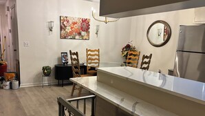 A modern kitchen with a marble countertop, wooden chairs, a stainless steel refrigerator, and a floral painting on the wall. - This home has been rented annually and not available on VRBO (Cape Coral)
