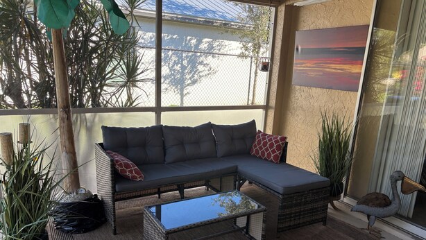 A covered patio area with a grey sectional sofa, a small coffee table, and potted plants. - This home has been rented annually and not available on VRBO (Cape Coral)