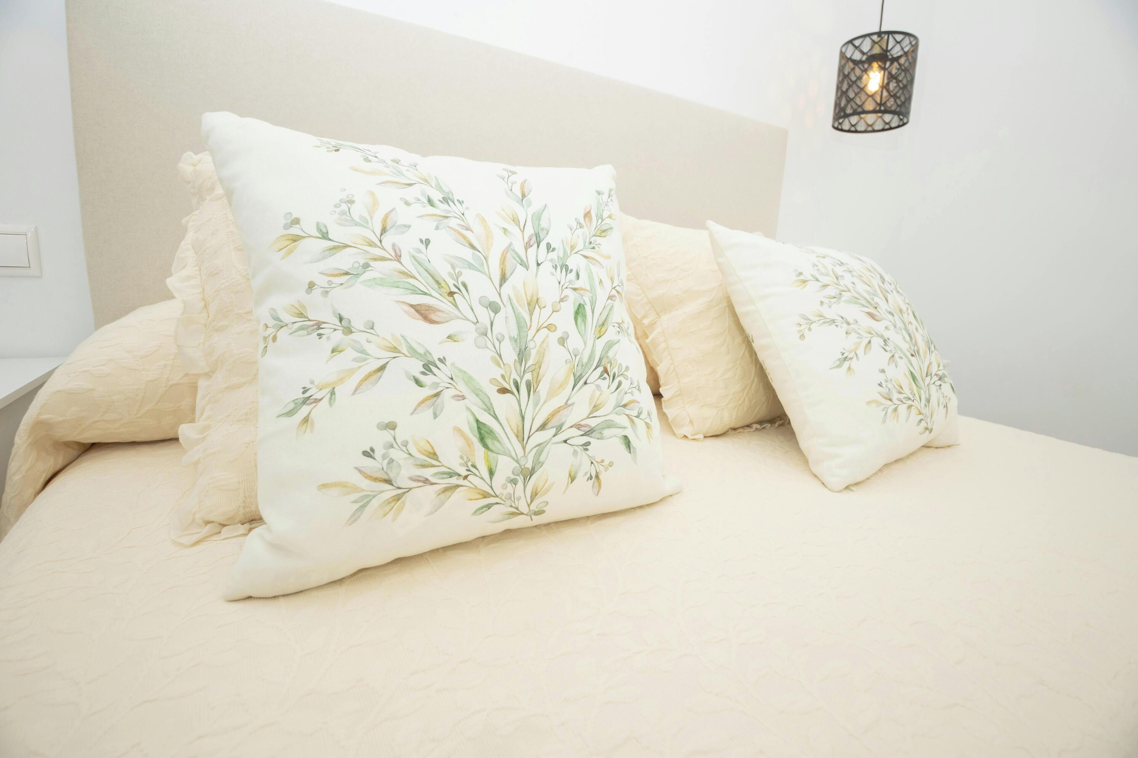 Ein Bett mit blumigen Kissen und einer gewebten, beige farbenen Tagesdecke.