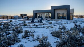 Una casa moderna con un ampio garage, un'area salotto esterna e un paesaggio innevato.