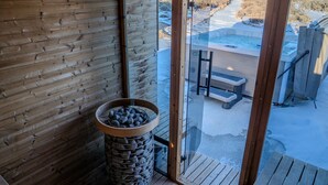 Un interno in legno con una ciotola di pietra, una porta in vetro che dà sull'esterno e vista su una vasca idromassaggio e area relax all'aperto.